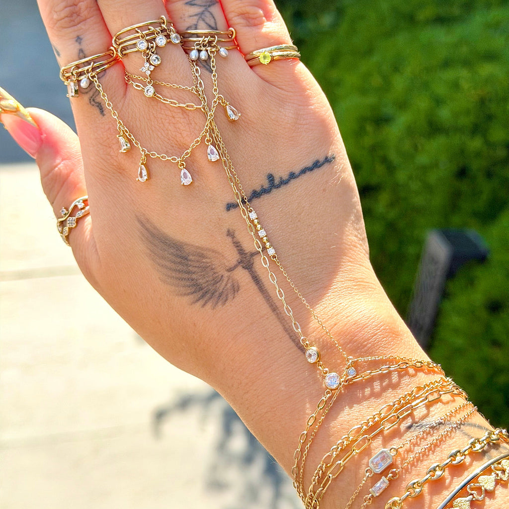 Hand wearing multiple gold rings and bracelets with a blurred outdoor background