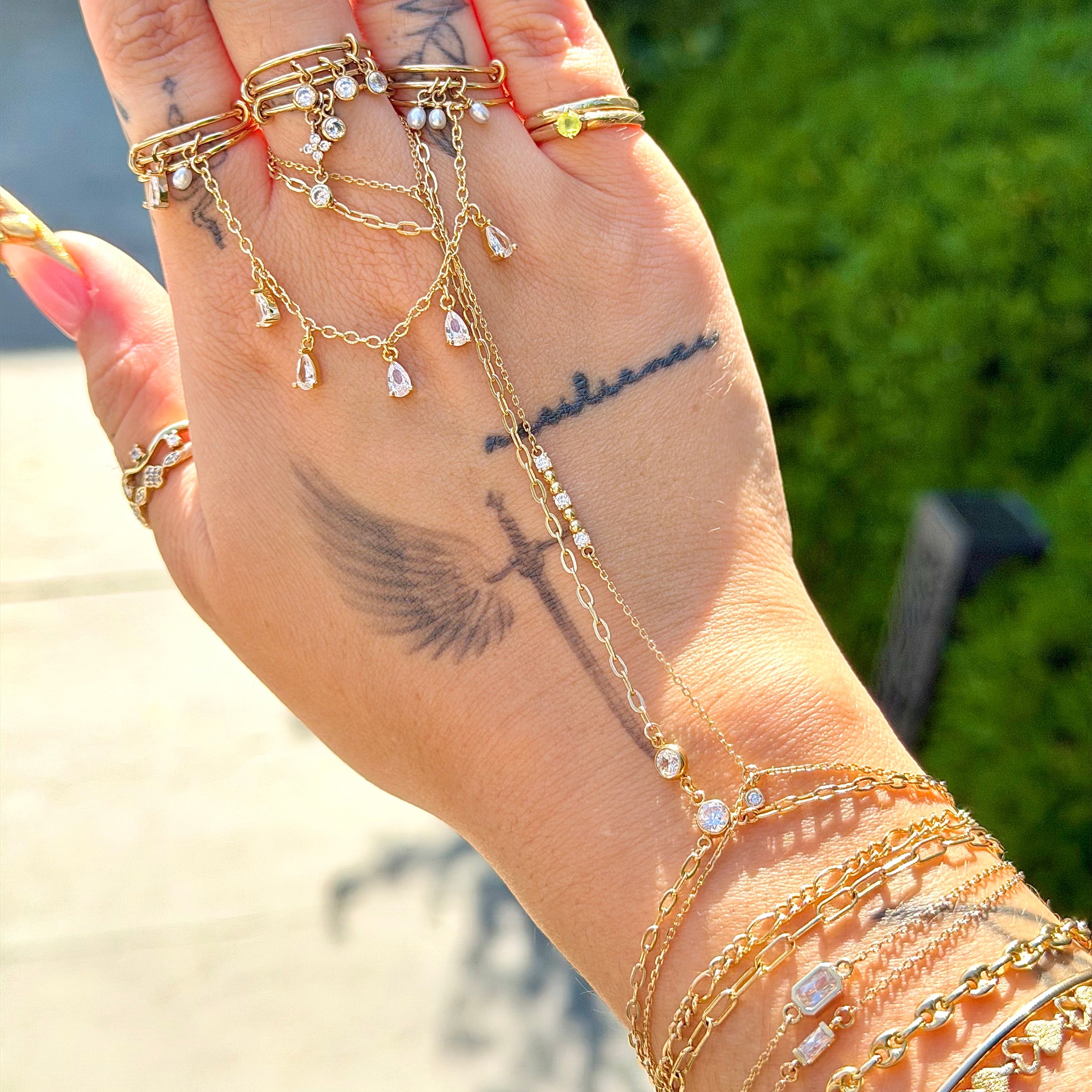 Hand wearing multiple gold rings and bracelets with a blurred outdoor background