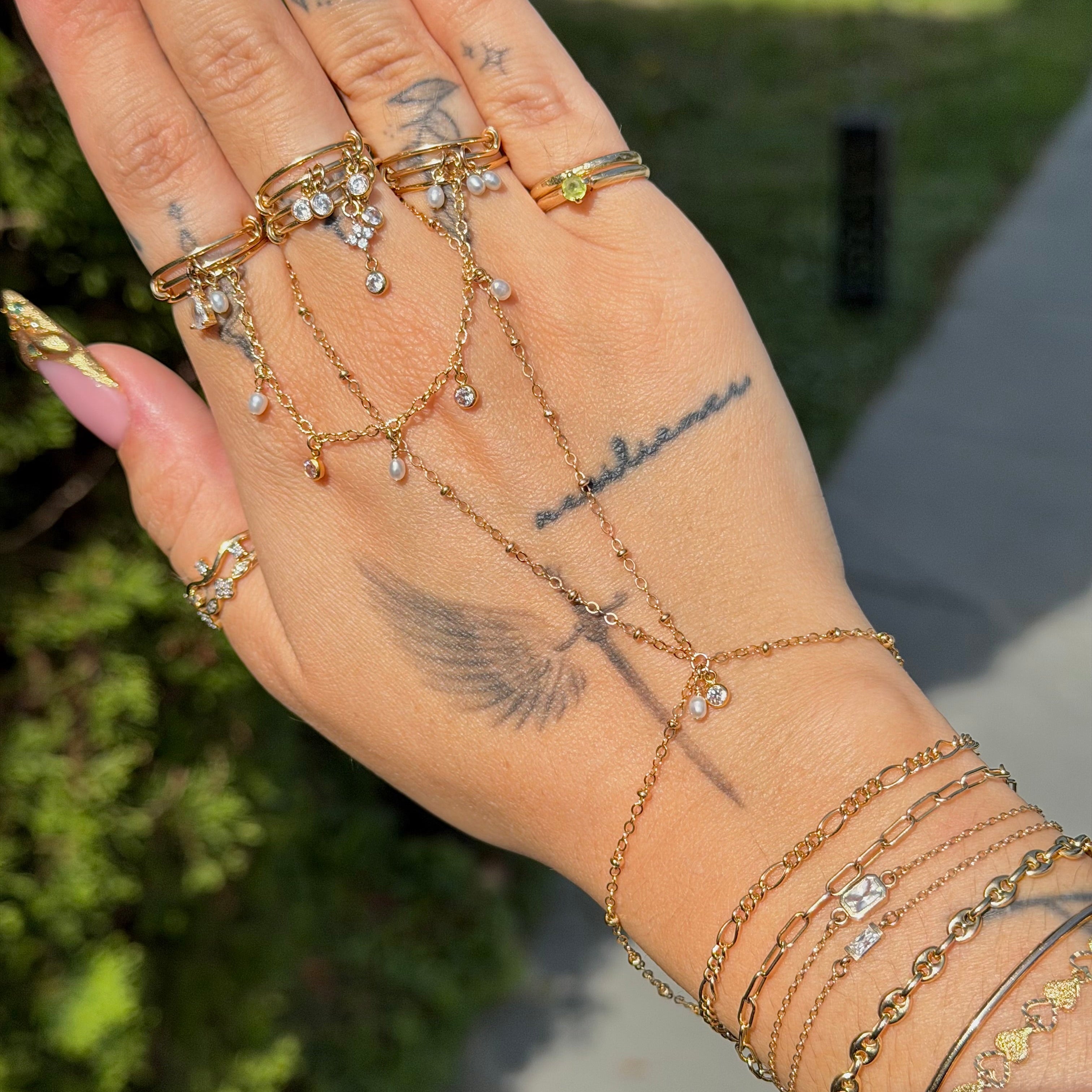 Hand wearing multiple gold and silver rings and bracelets with tattoos on a blurred natural background