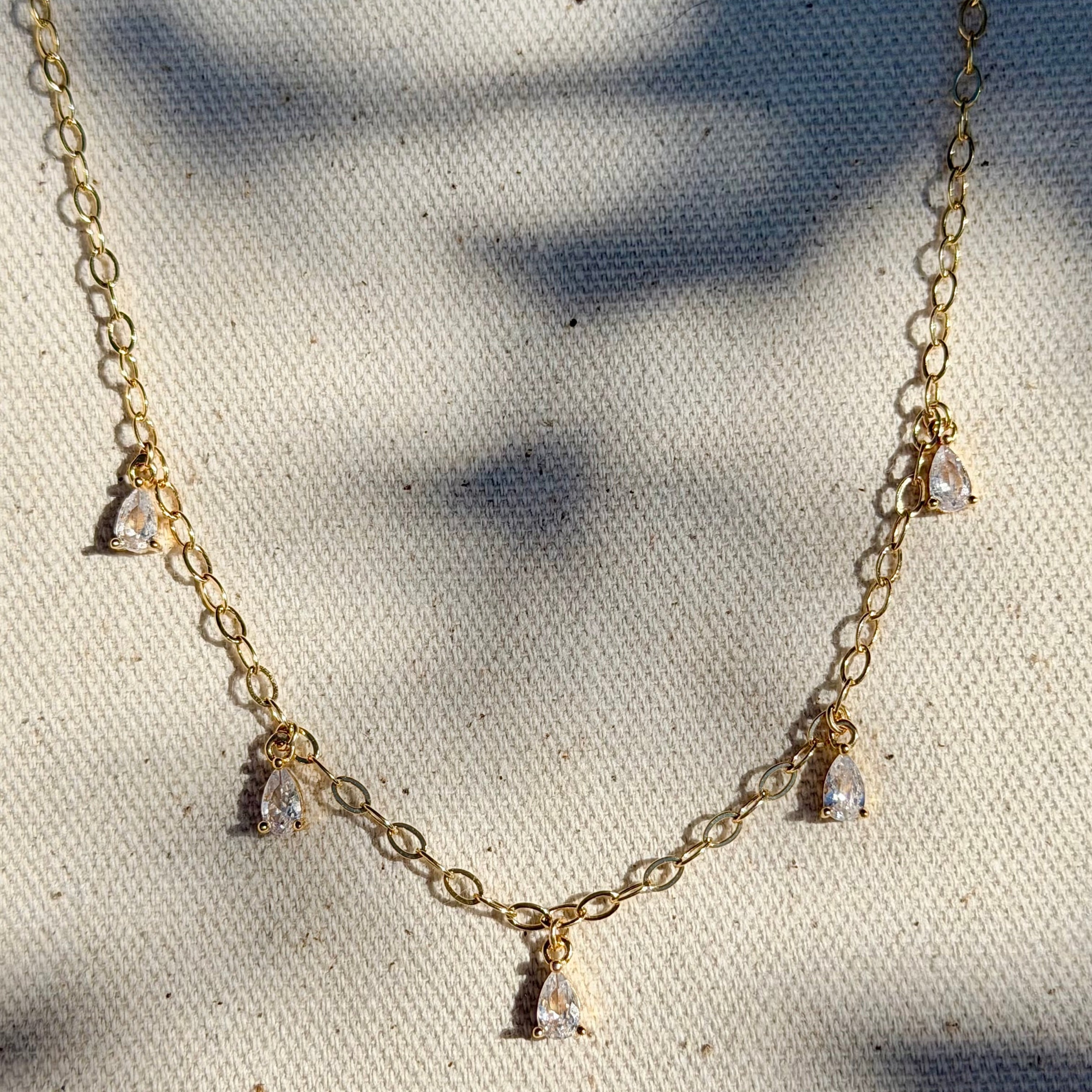 Gold necklace with small pendants on a textured white surface