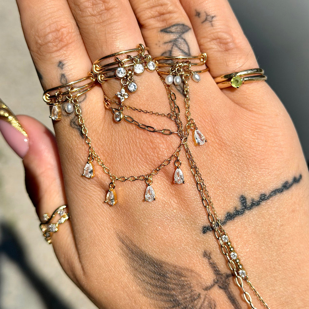 Hand wearing multiple gold rings with gemstones on a neutral background
