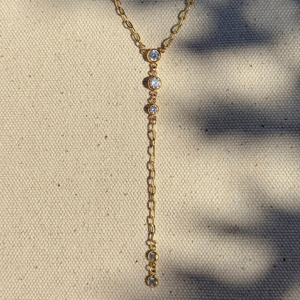 Gold necklace with small stones on a textured beige surface