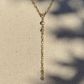 Gold necklace with small stones on a textured beige surface