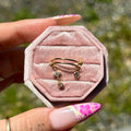 Pink velvet jewelry box with gold earrings held by a hand with floral nail polish.