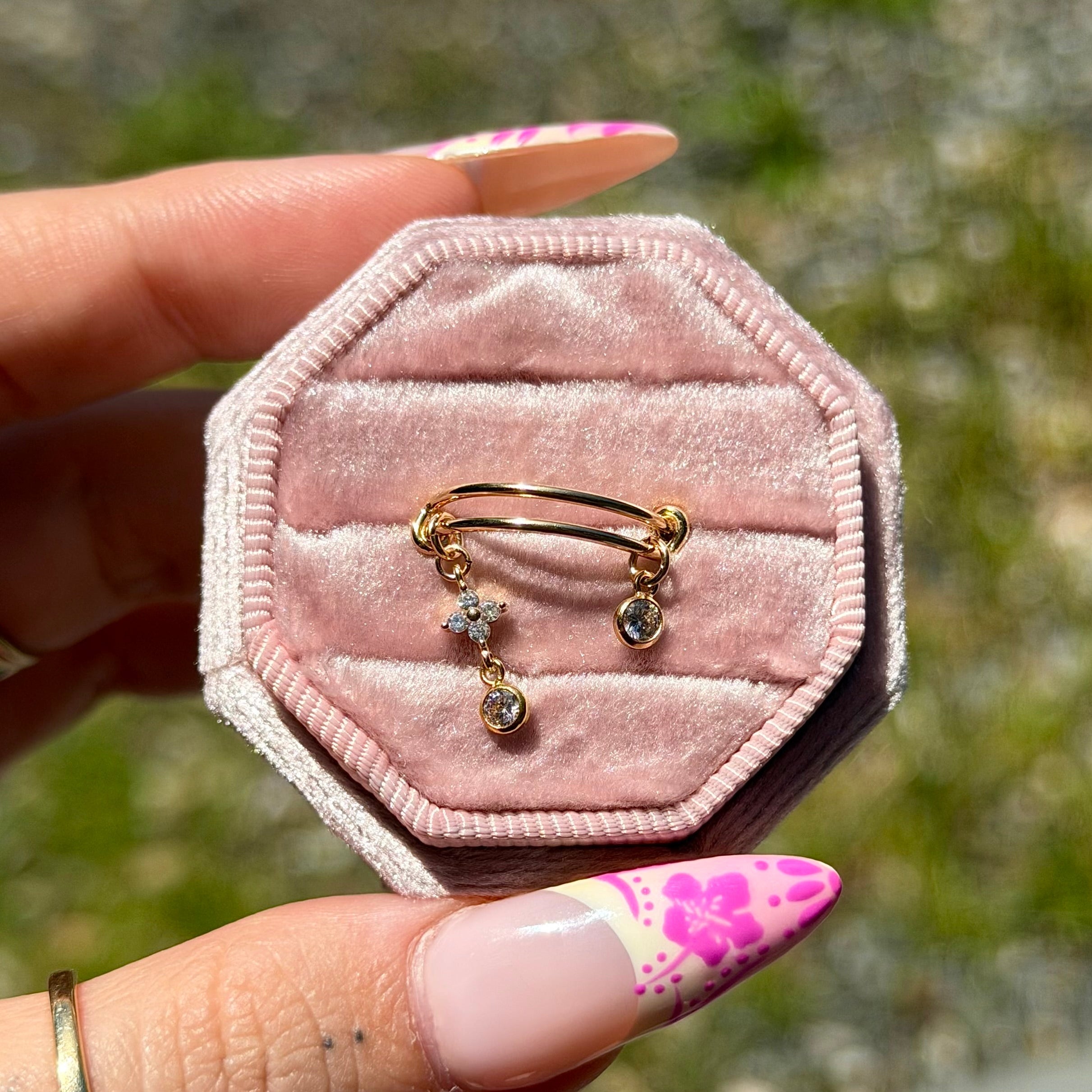 Pink velvet jewelry box with gold earrings held by a hand with floral nail polish.