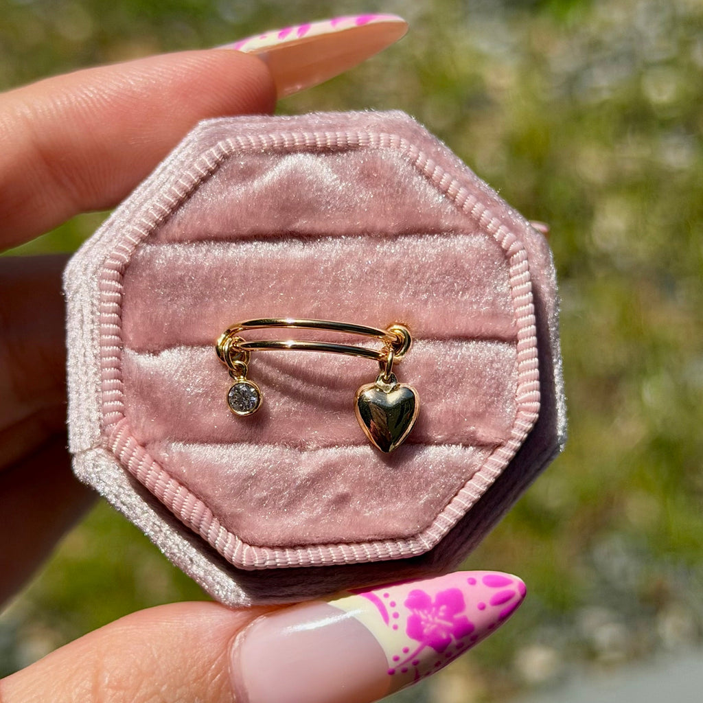 Hexagonal pink velvet jewelry box with two gold rings, held by a hand with floral nail polish.