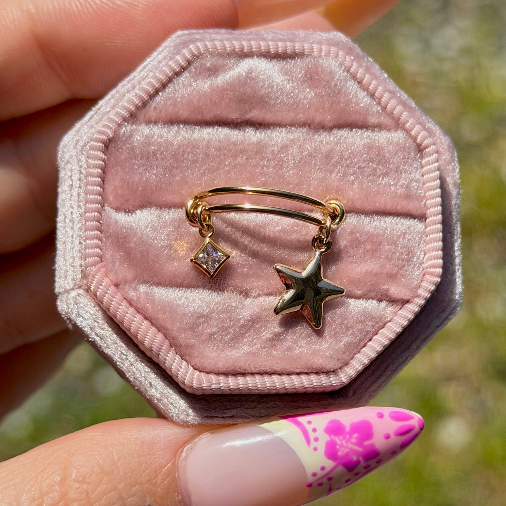 Hexagonal pink velvet jewelry box with gold ring featuring star and diamond charm.
