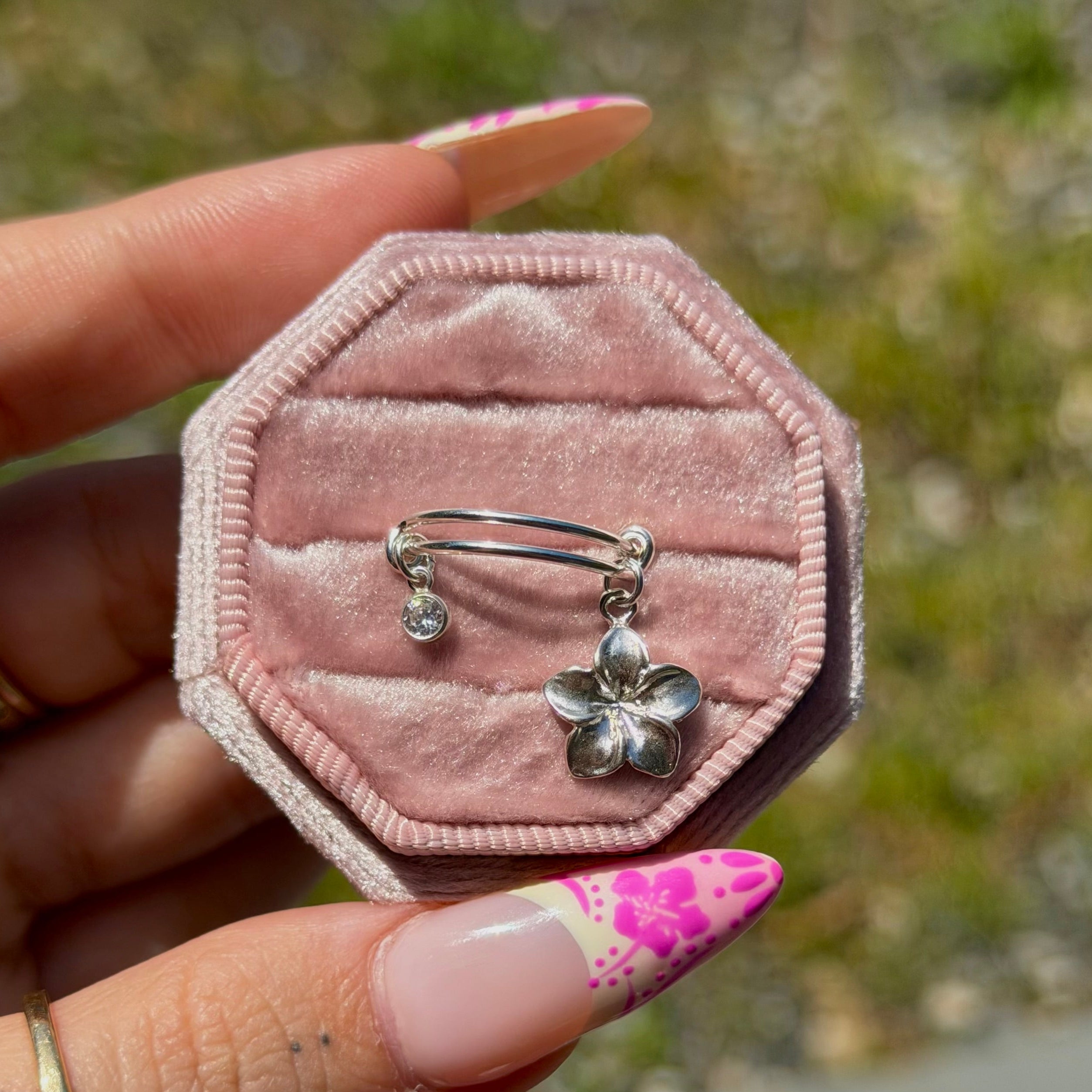 Pink hexagonal jewelry box with silver earrings held by a hand against a blurred natural background