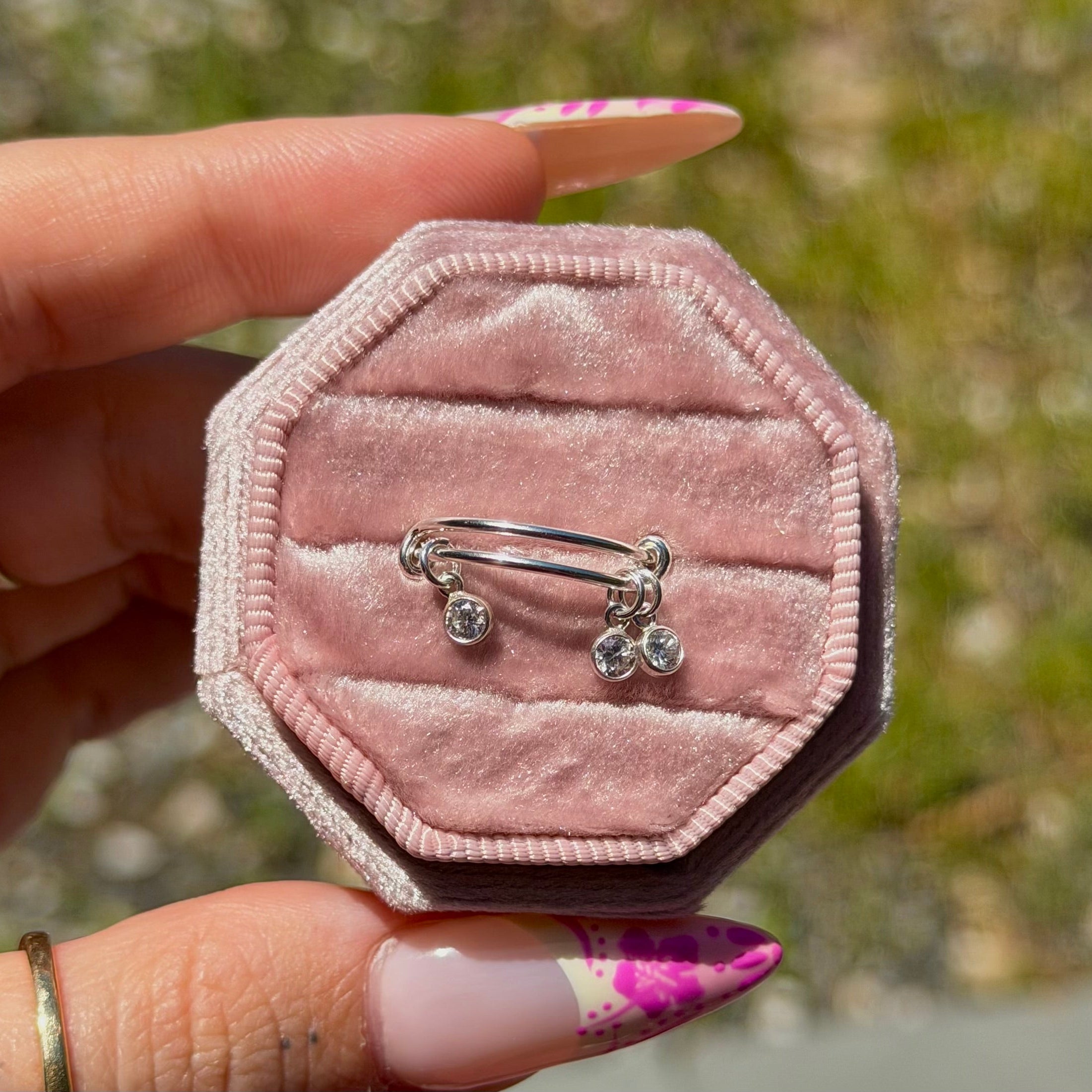 Hexagonal pink velvet jewelry box with a ring inside, held by a hand against a blurred natural background.