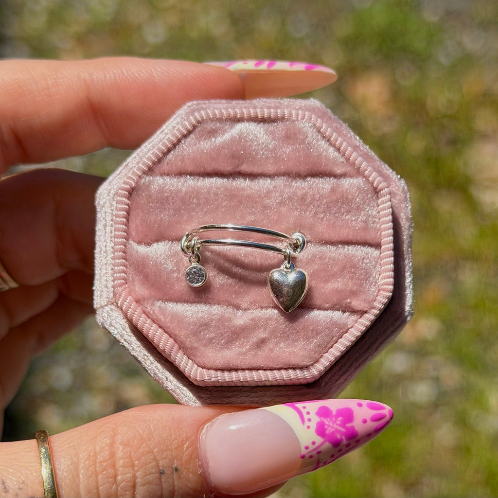 Pink velvet jewelry box with silver rings held by a hand against a blurred natural background