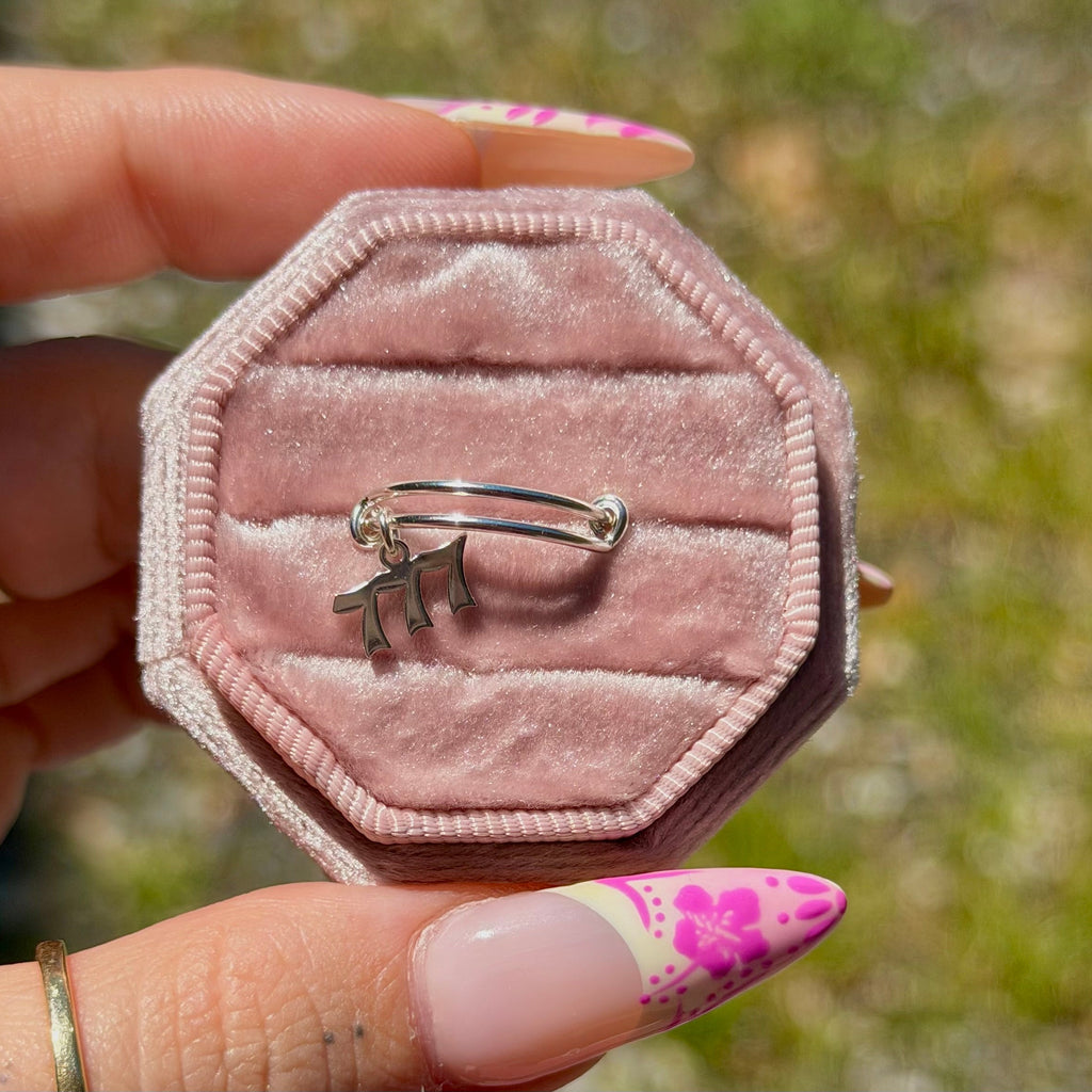 Hexagonal pink velvet jewelry box with a silver ring held by a hand with floral nail polish.