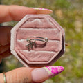 Hexagonal pink velvet jewelry box with a silver ring held by a hand with floral nail polish.