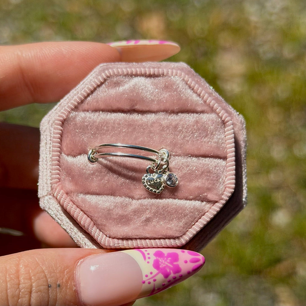 Hand holding a pink hexagonal jewelry box with a silver ring featuring a heart and diamond design.