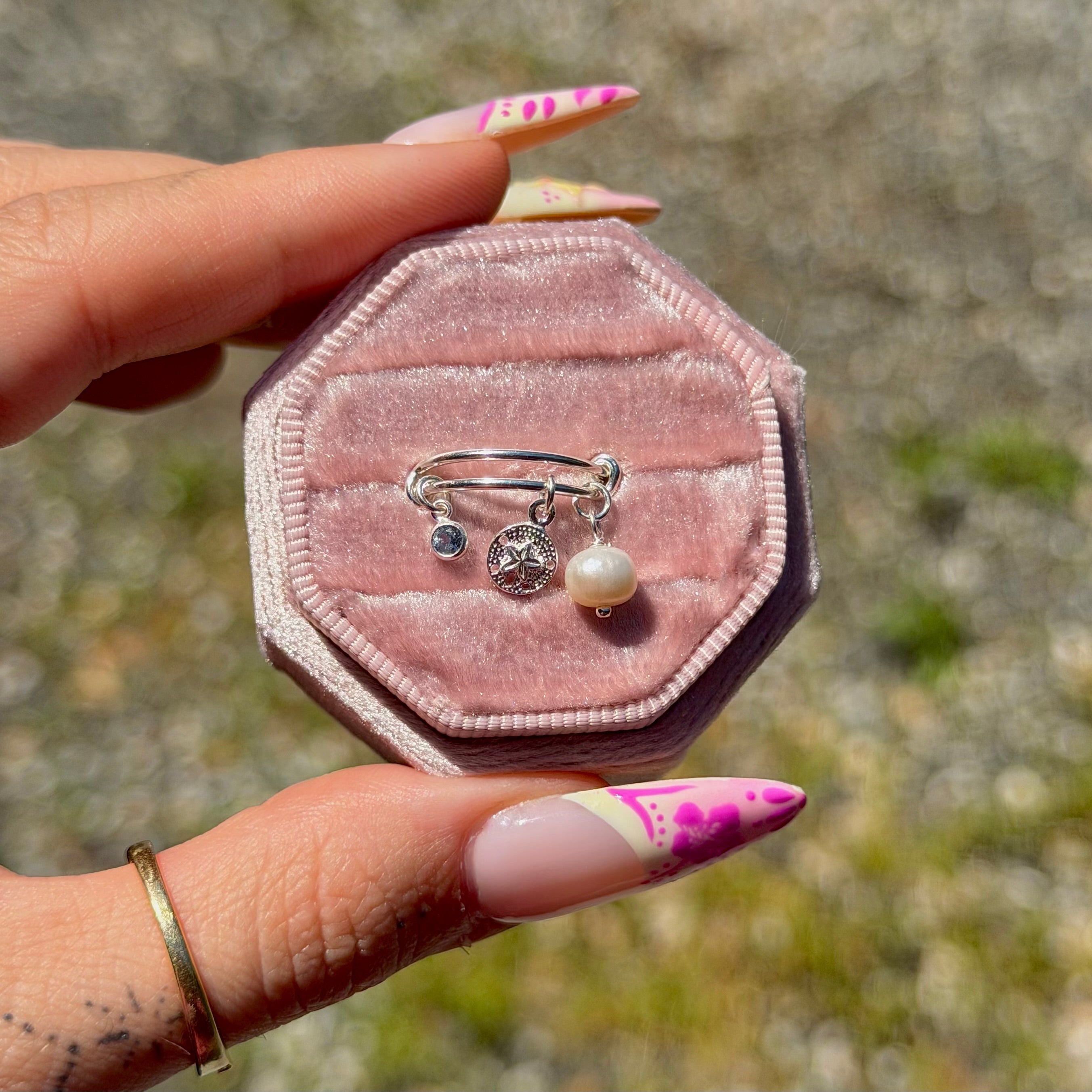 Pink velvet jewelry box with rings held by a hand against a natural background