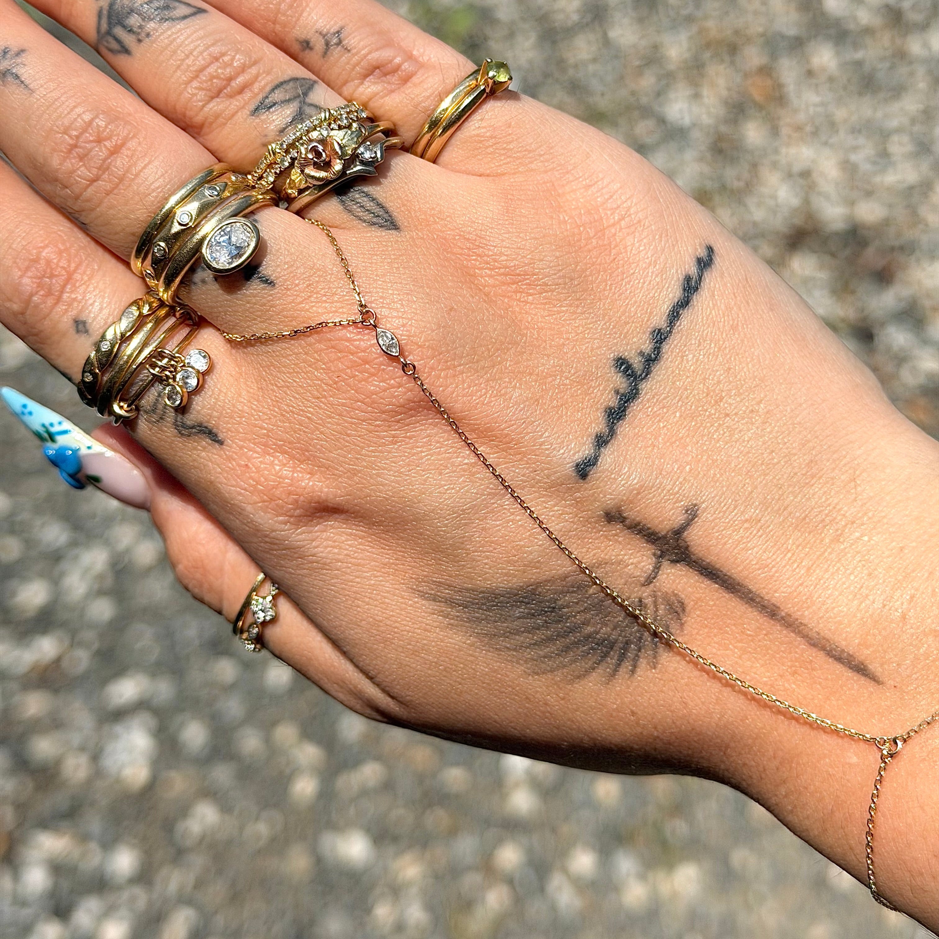 Hand with multiple gold rings and tattoos on a textured surface