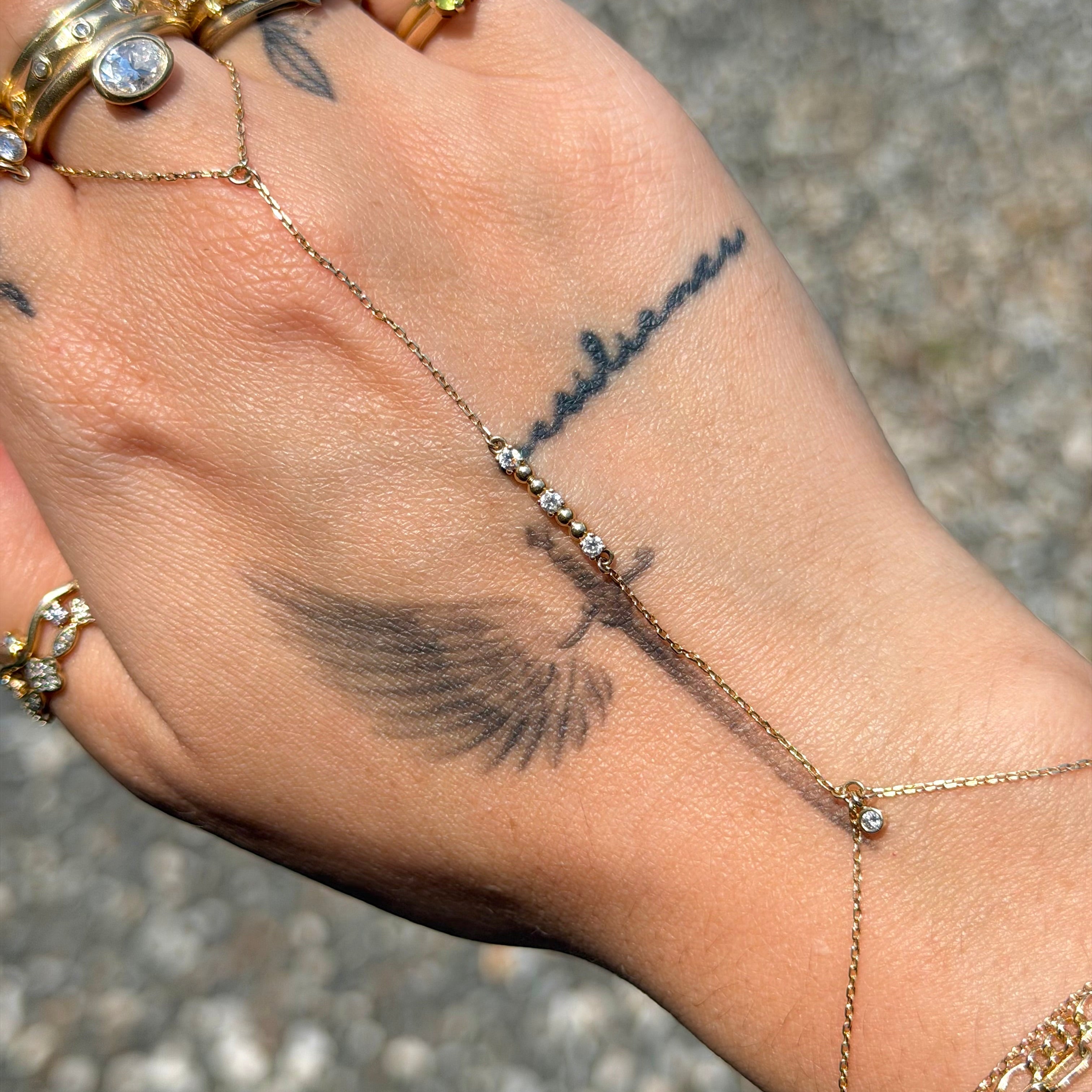 Hand with gold rings and bracelets, featuring a tattoo on the palm.