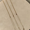 Three gold necklaces on a beige fabric background