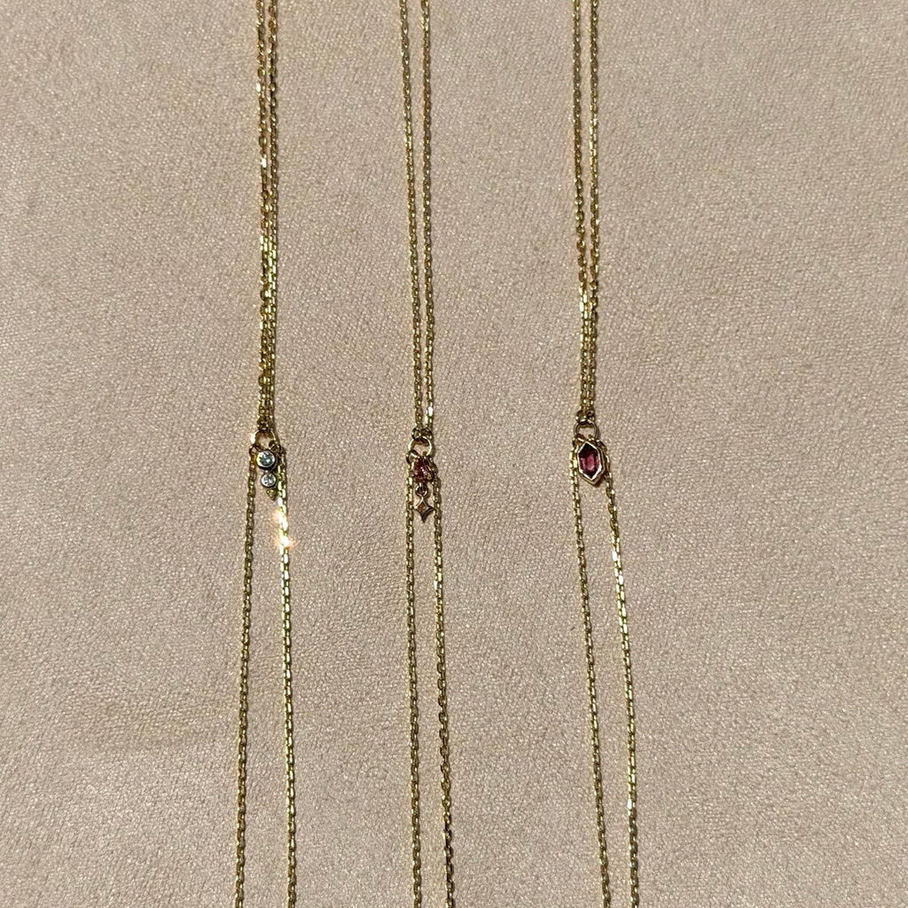 Three gold necklaces with gemstone pendants on a beige background
