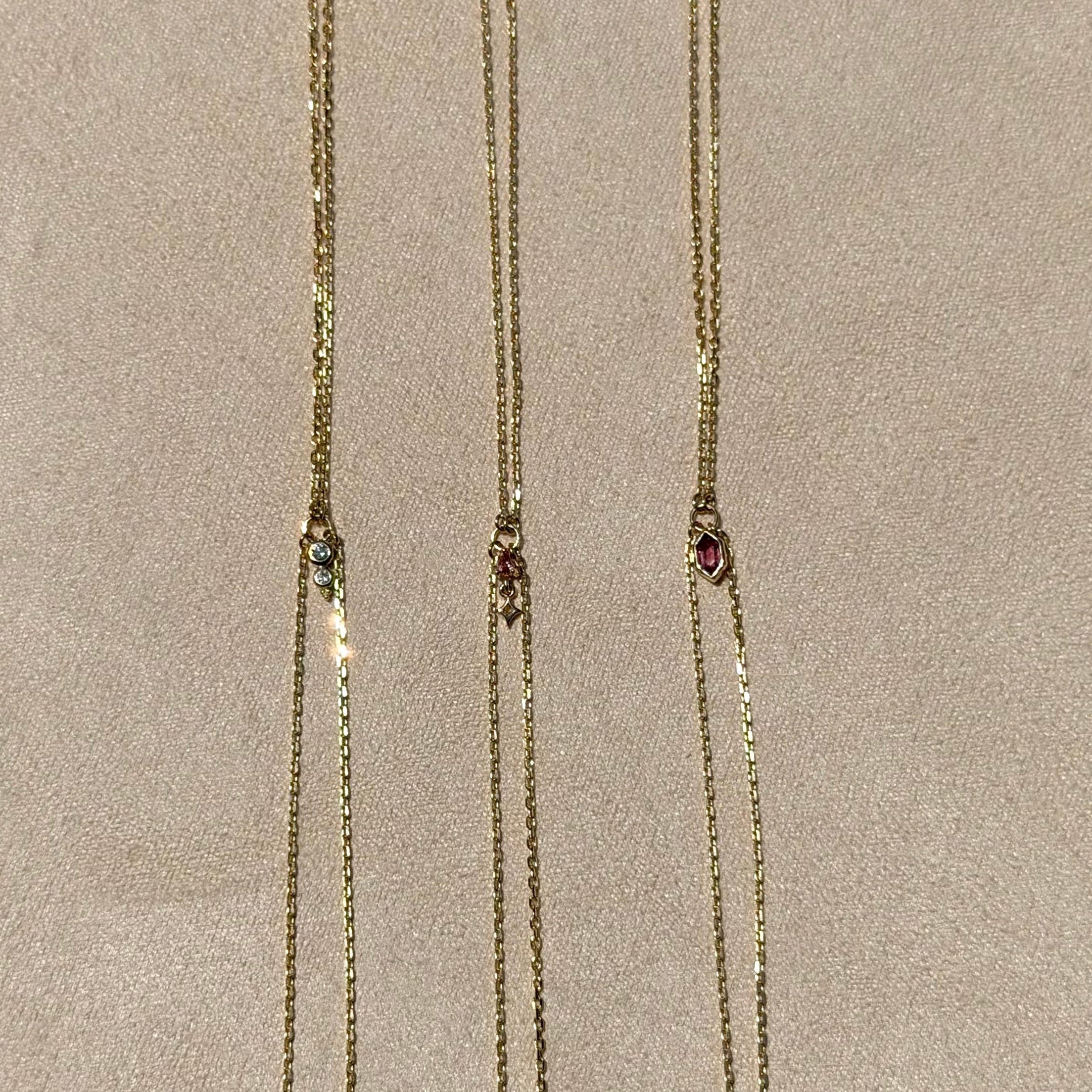 Three gold necklaces with gemstone pendants on a beige background
