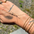 Hand with gold bracelets and rings against a blurred outdoor background