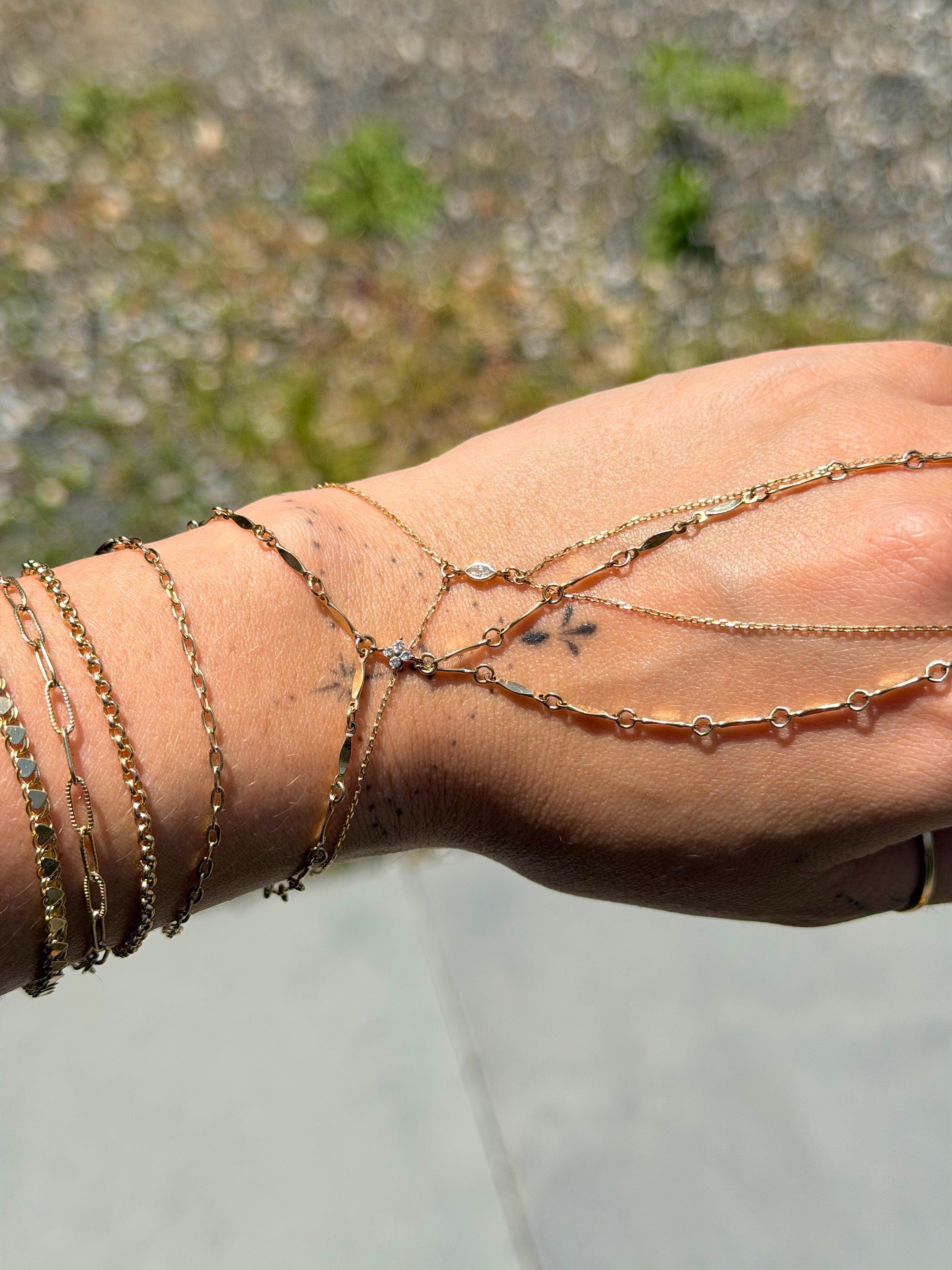 Close-up of a wrist with multiple gold bracelets against a blurred natural background