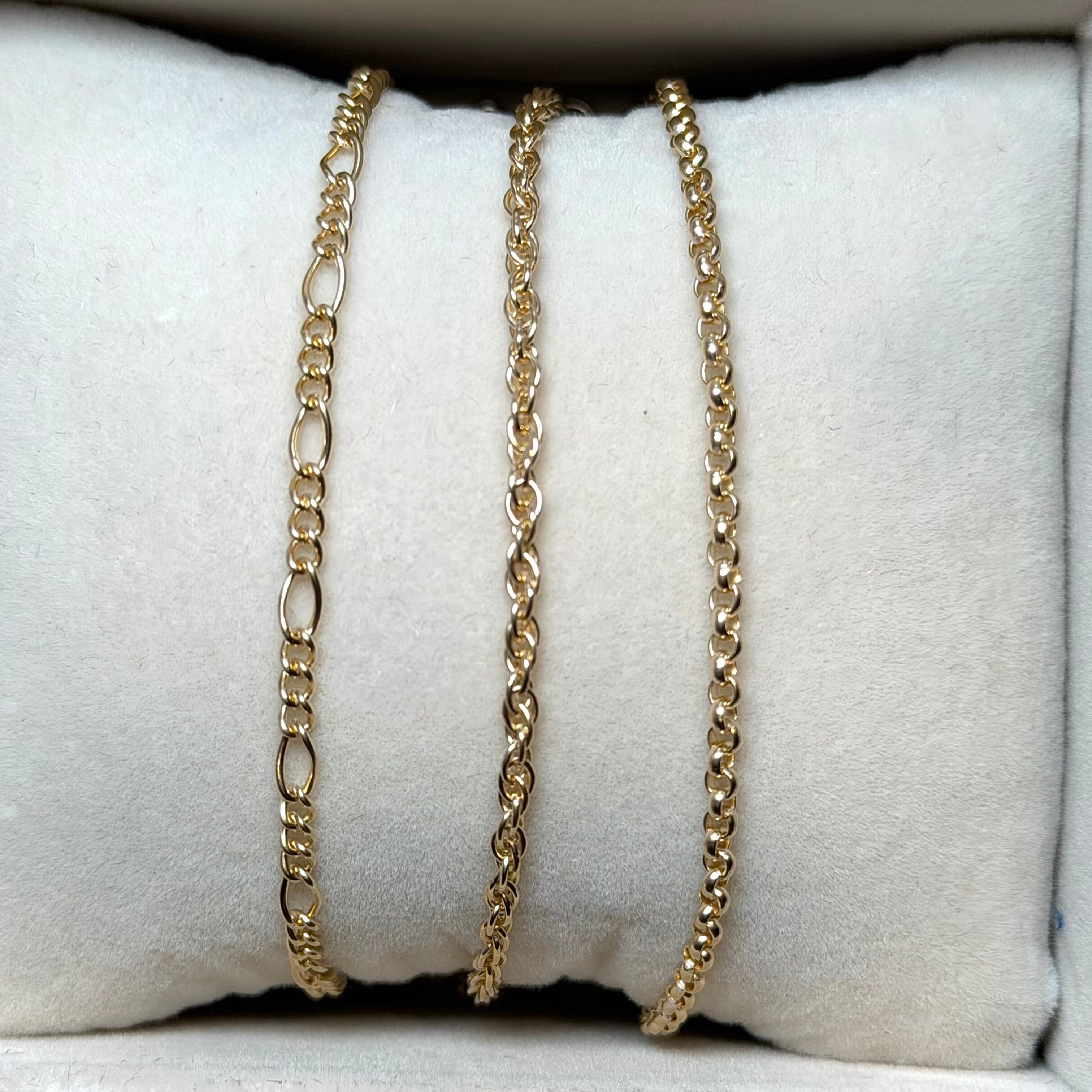 Gold and silver chain necklaces on a white cushioned surface