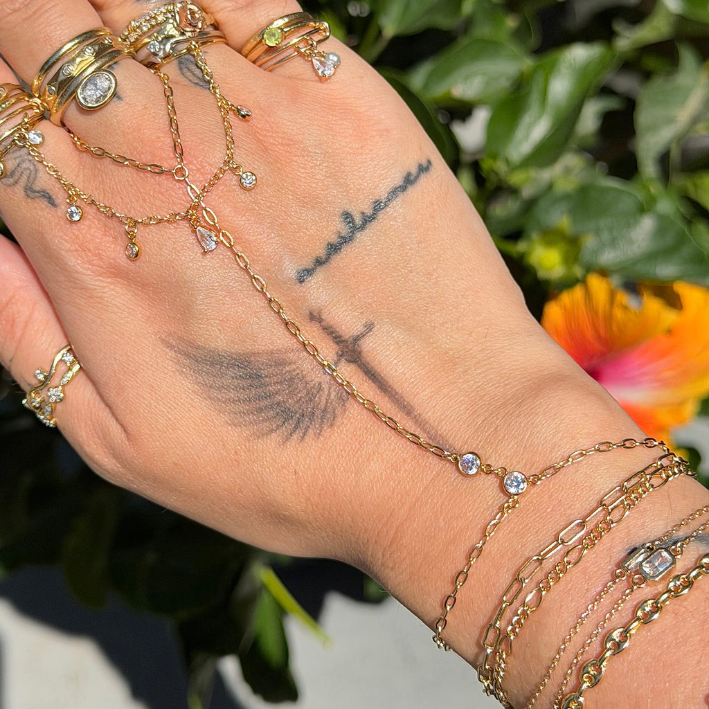 Hand wearing multiple gold rings and bracelets with a blurred natural background