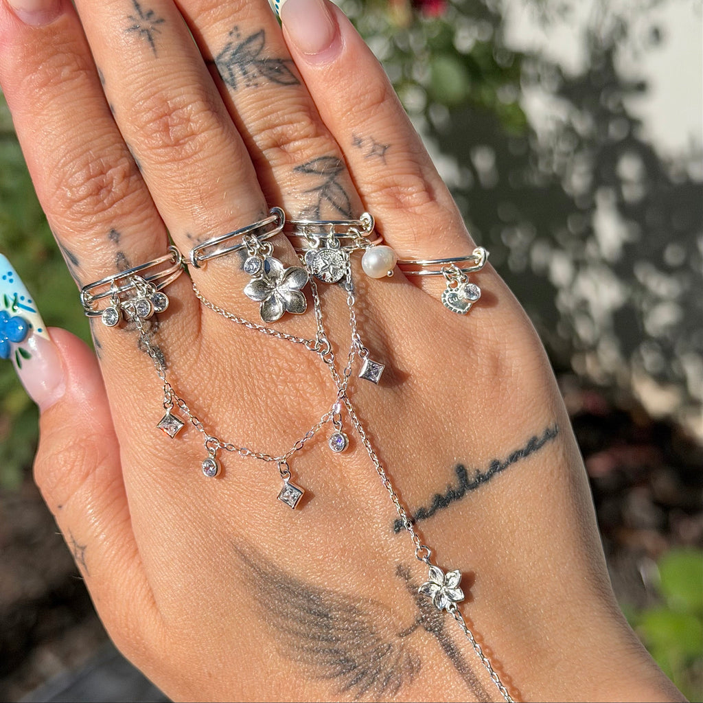 Hand wearing multiple silver rings with floral and chain designs against a blurred natural background.