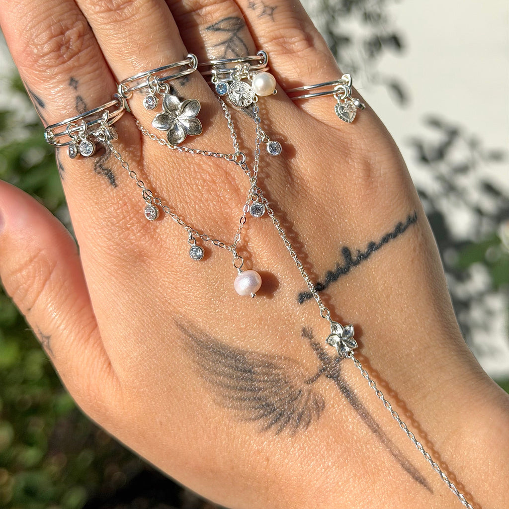 Hand wearing multiple silver rings with floral and star designs against a blurred natural background