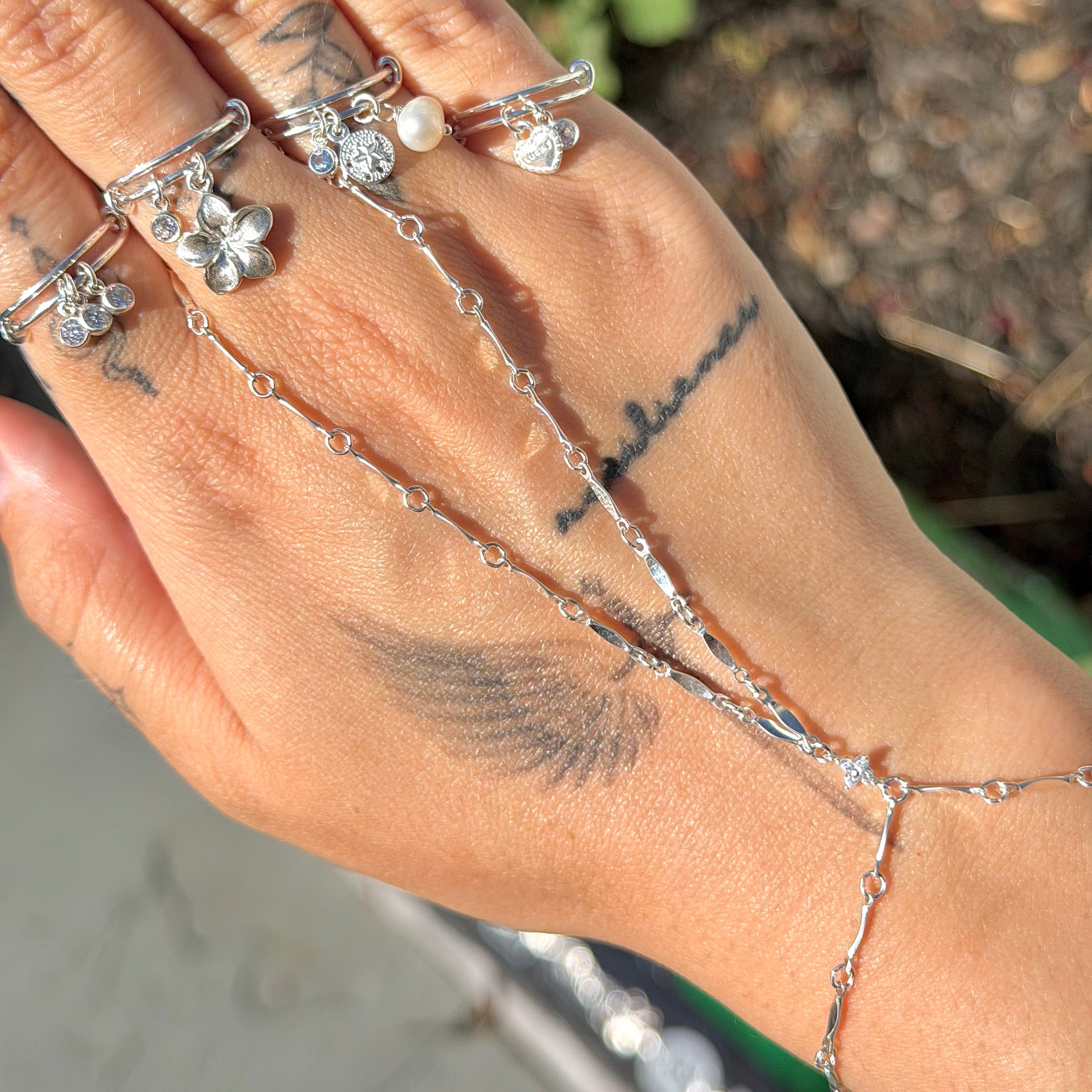 Hand wearing multiple silver rings with a blurred outdoor background