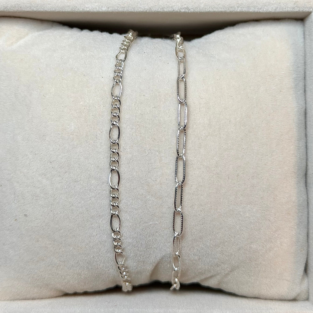 Two silver chain bracelets on a textured white surface