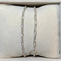 Two silver chain bracelets on a textured white surface