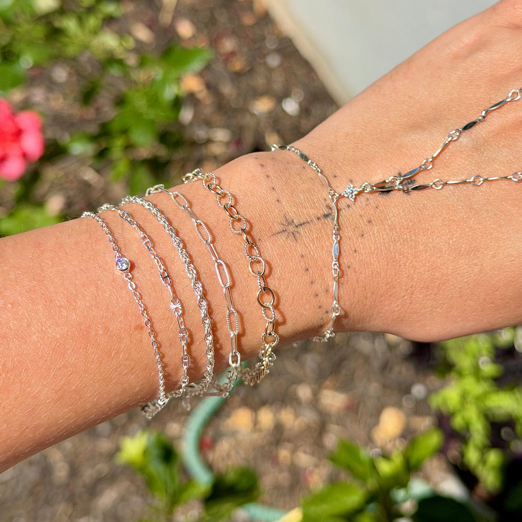 Close-up of a wrist wearing multiple silver bracelets with a blurred natural background