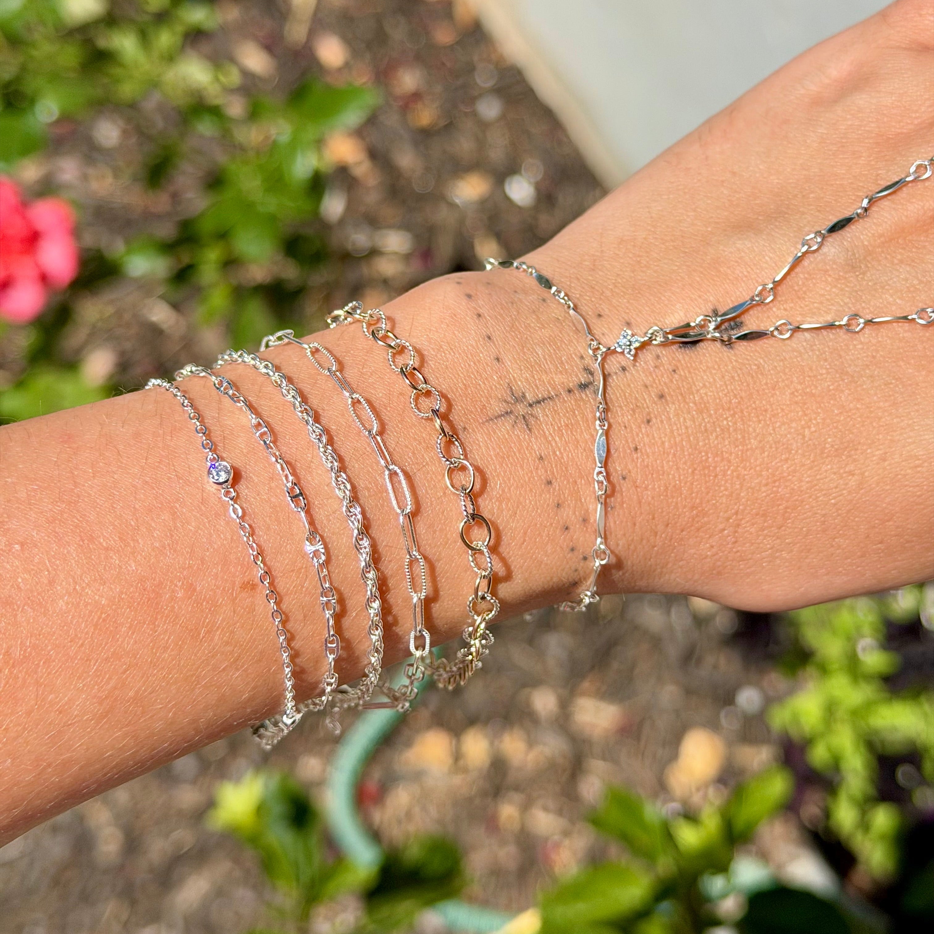 Close-up of a wrist wearing multiple silver bracelets with a blurred natural background