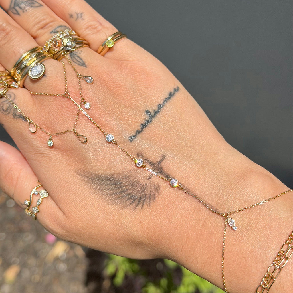 Hand wearing multiple gold rings and bracelets with a blurred natural background
