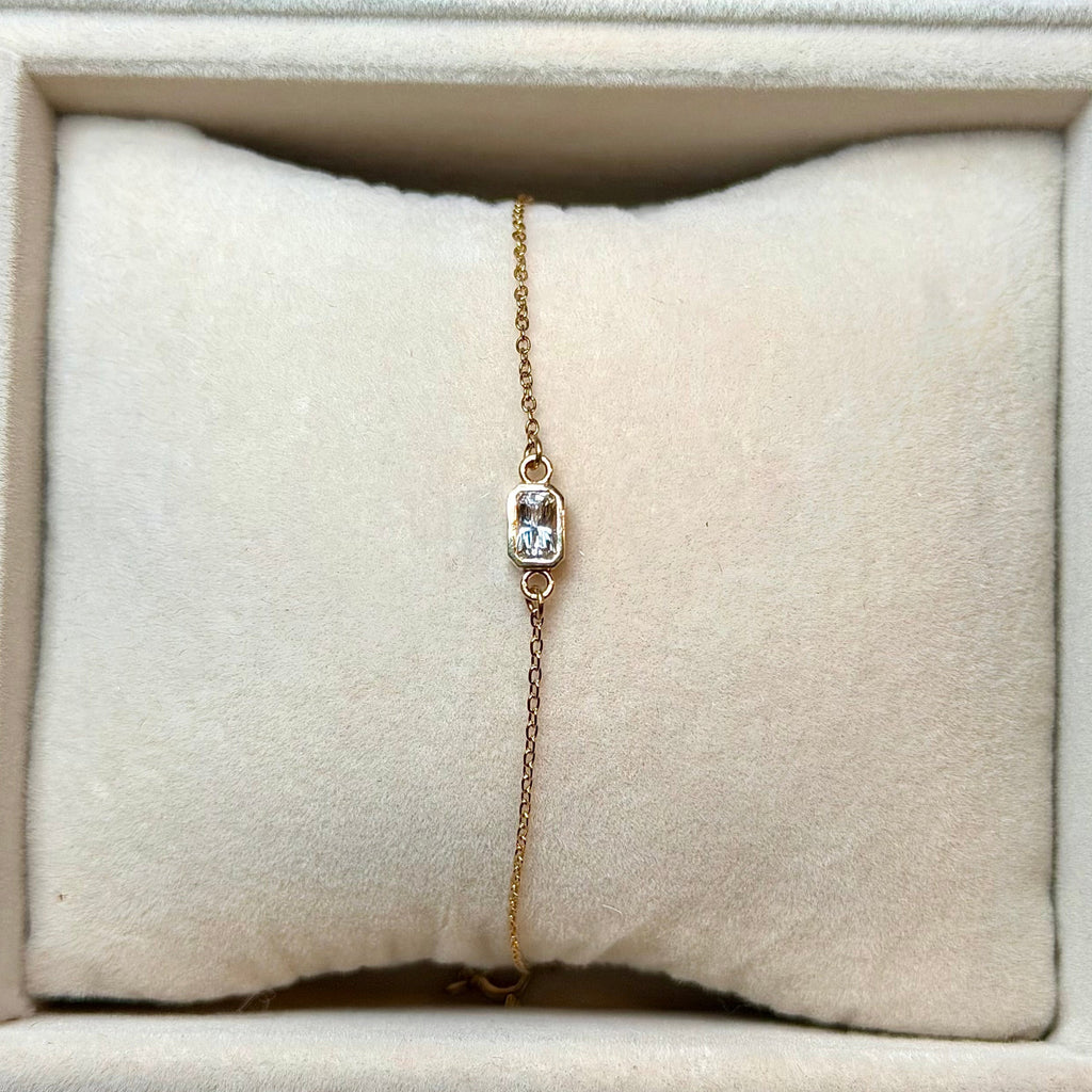 Gold bracelet with a diamond on a beige cushion in a jewelry display case.