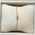 Gold bracelet with a diamond on a beige cushion in a jewelry display case.